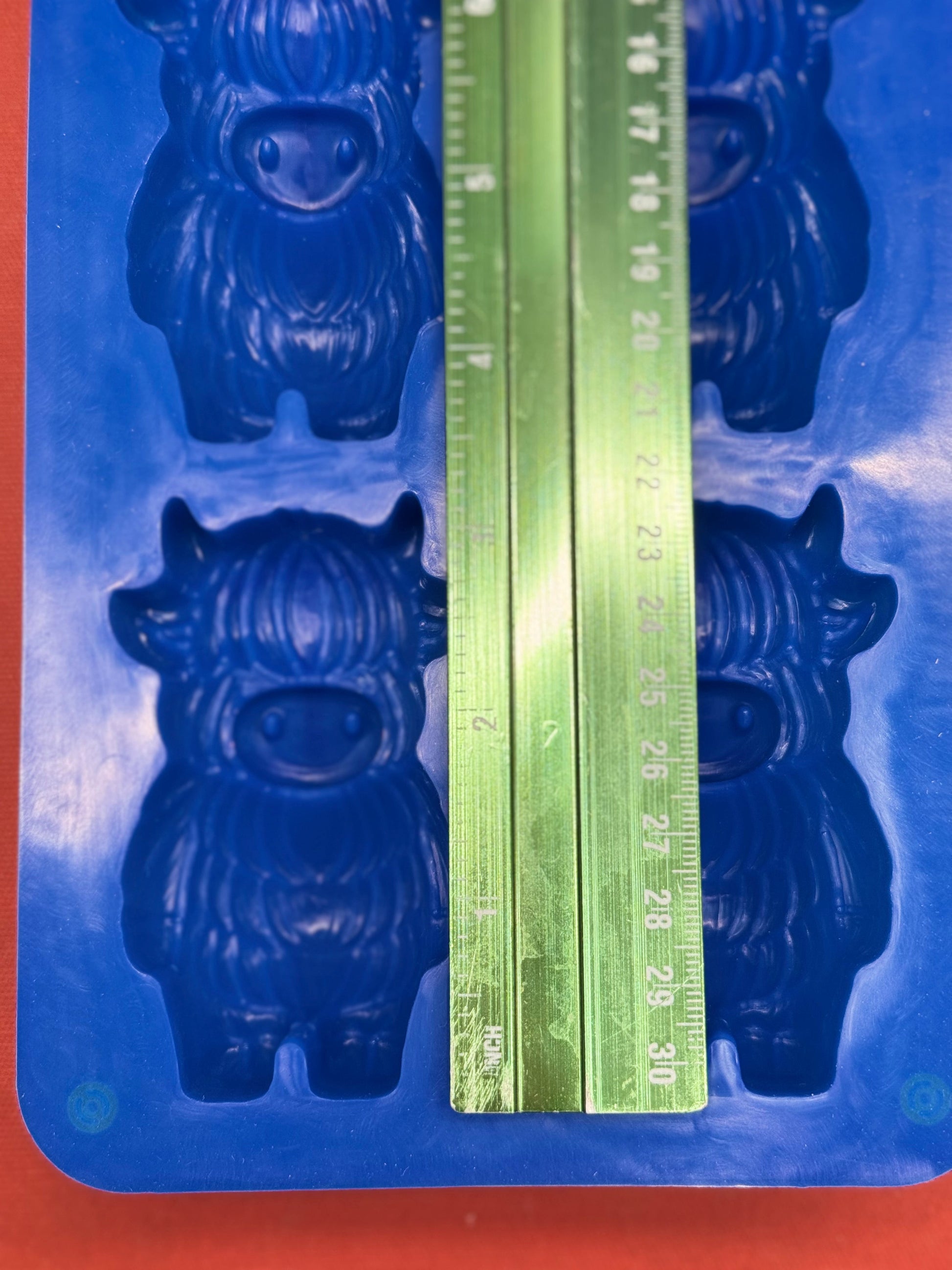Blue mold with cow shape and a green ruler for measurement on an orange background