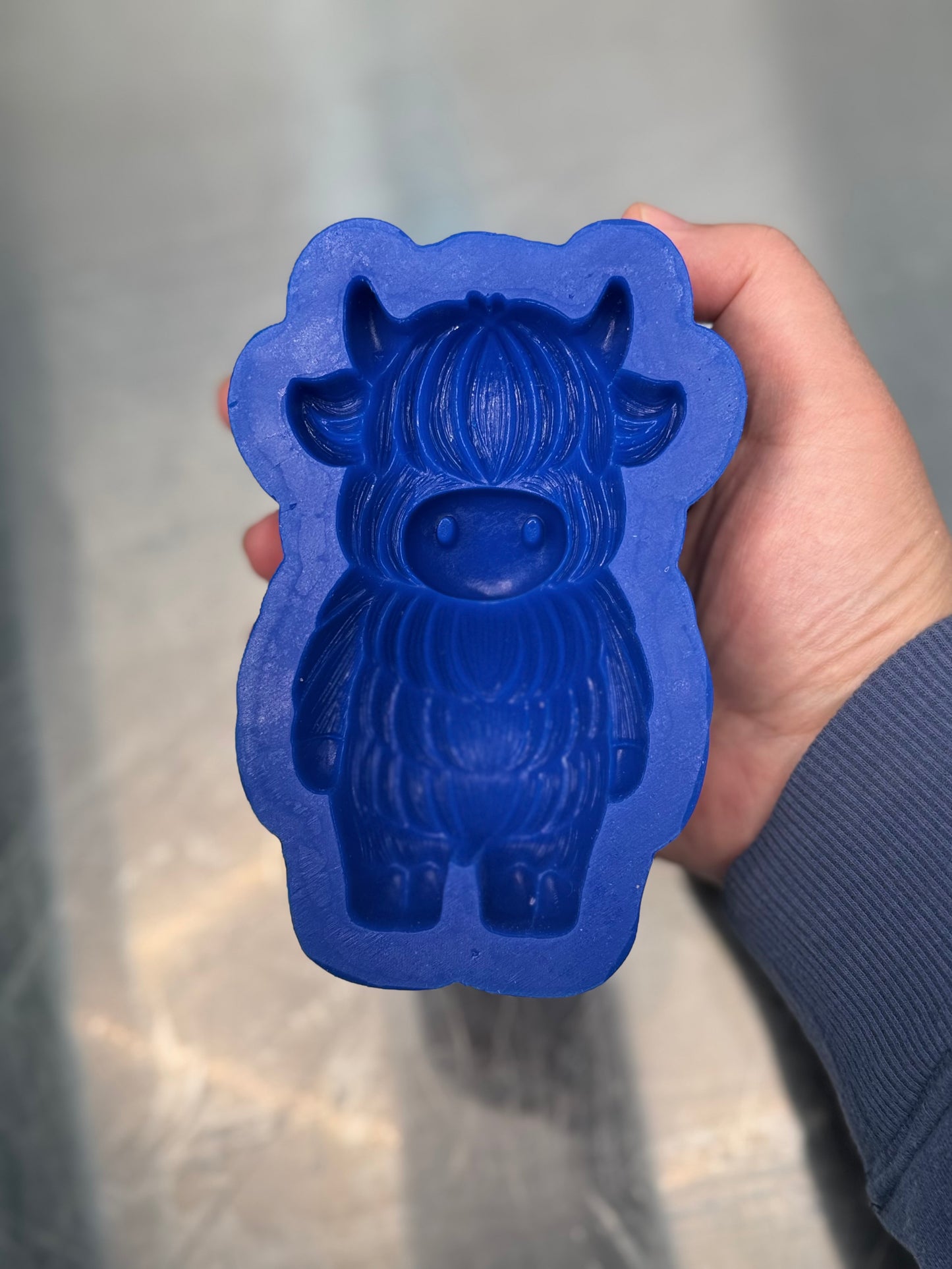 Blue cow-shaped mold held by a hand against a neutral background
