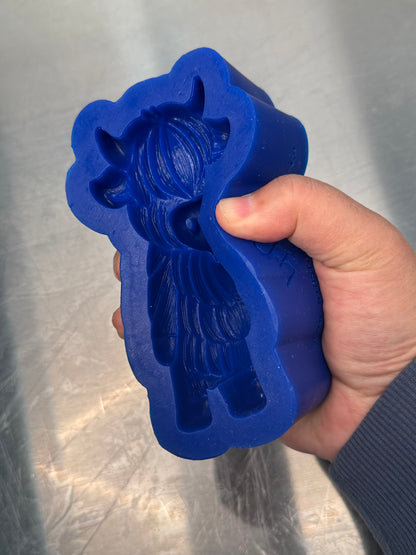 Blue silicone mold shaped like a cow held by a hand against a metallic background