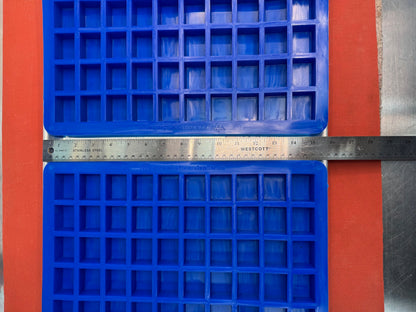 Two blue silicone mold with square compartments on an orange background, measured by a ruler.