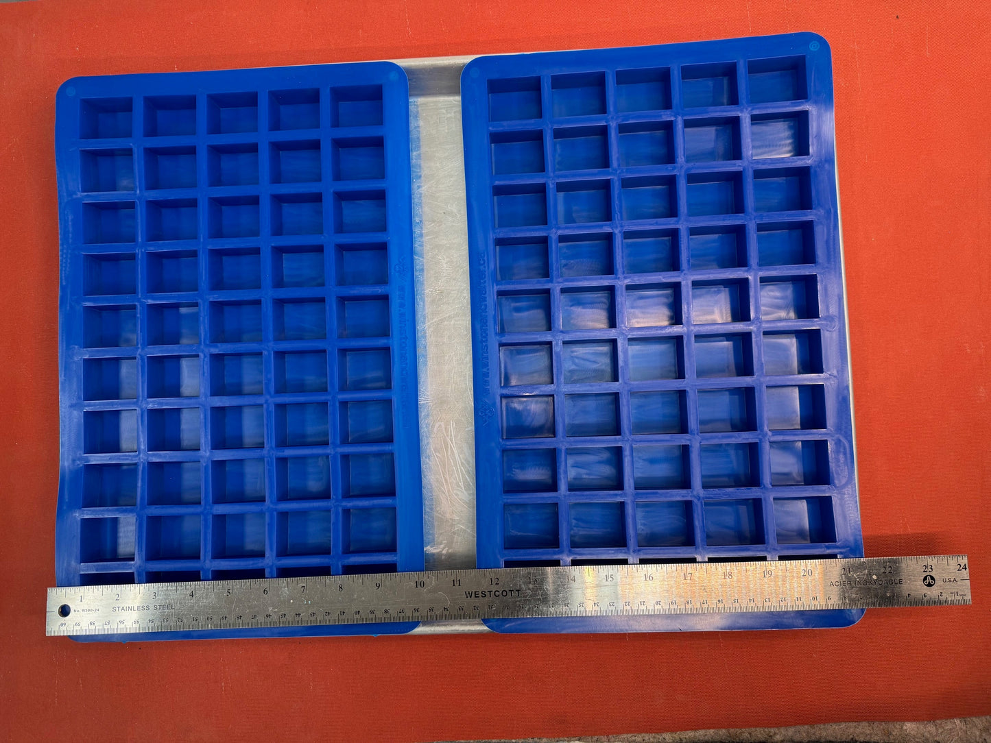 Two blue silicone mold with square compartments on an orange background, measured by a ruler.