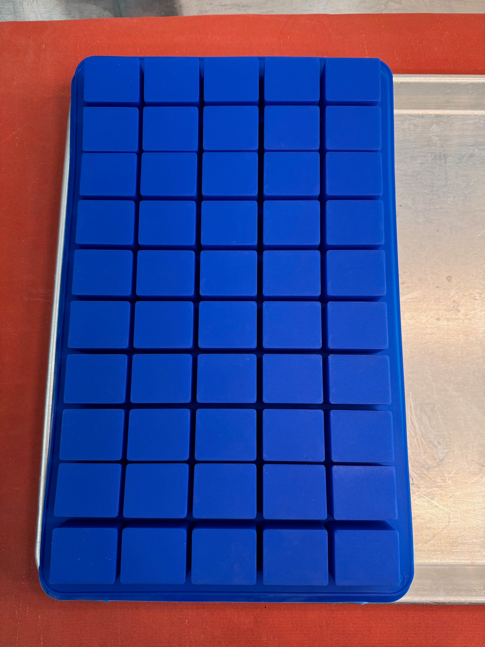 Flat bottom blue silicone cavity mold with square compartments on an orange background